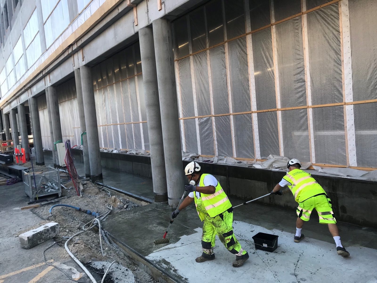 Two KBT operatives rolling PAR1 primer onto the podium deck in front of the row of columns