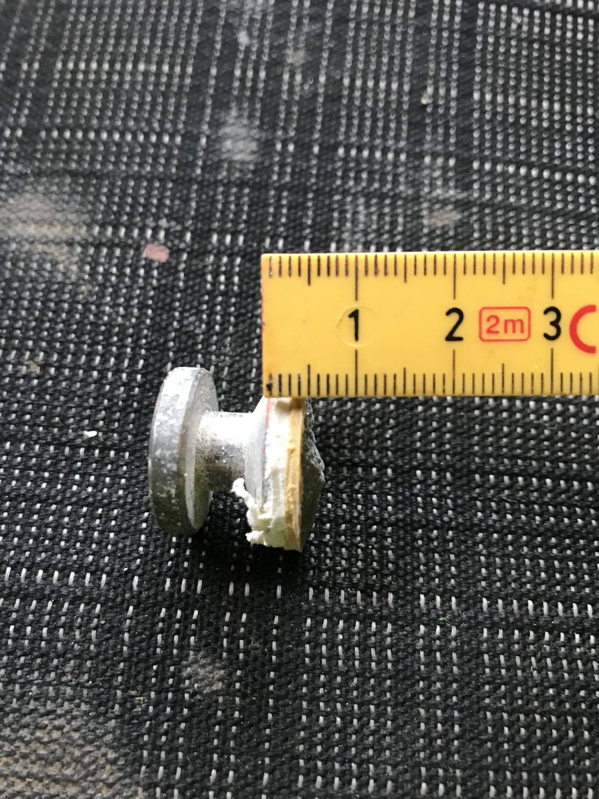 Prøvestempel med gult og hvidt membranlag oven på beton, målt med tommestok