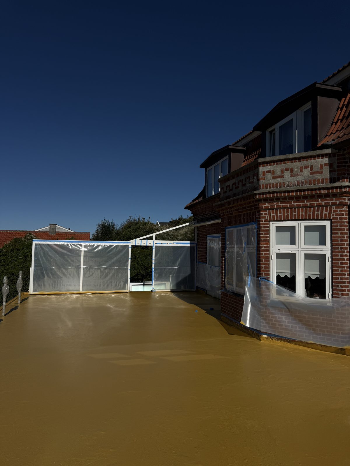 Færdigsprøjtet gul Eliminator-membran over hele terrassen med afdækkede vinduer og glasværn